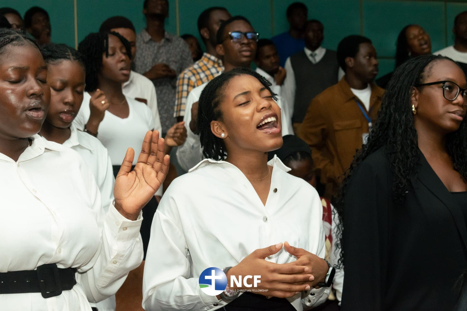 Students in white shirts worshipping, one with a hand raised