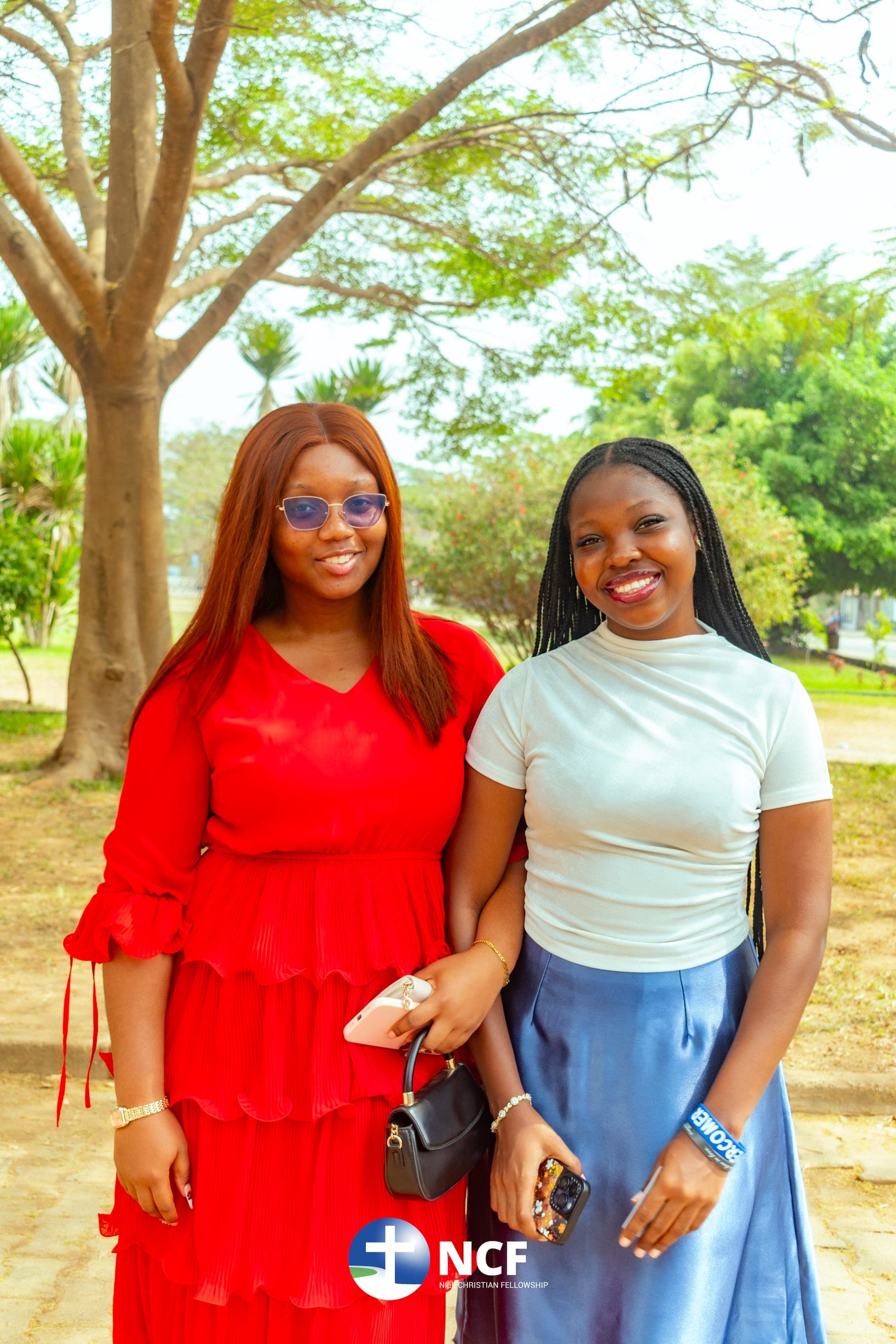 Two students smiling together under a tree on campus