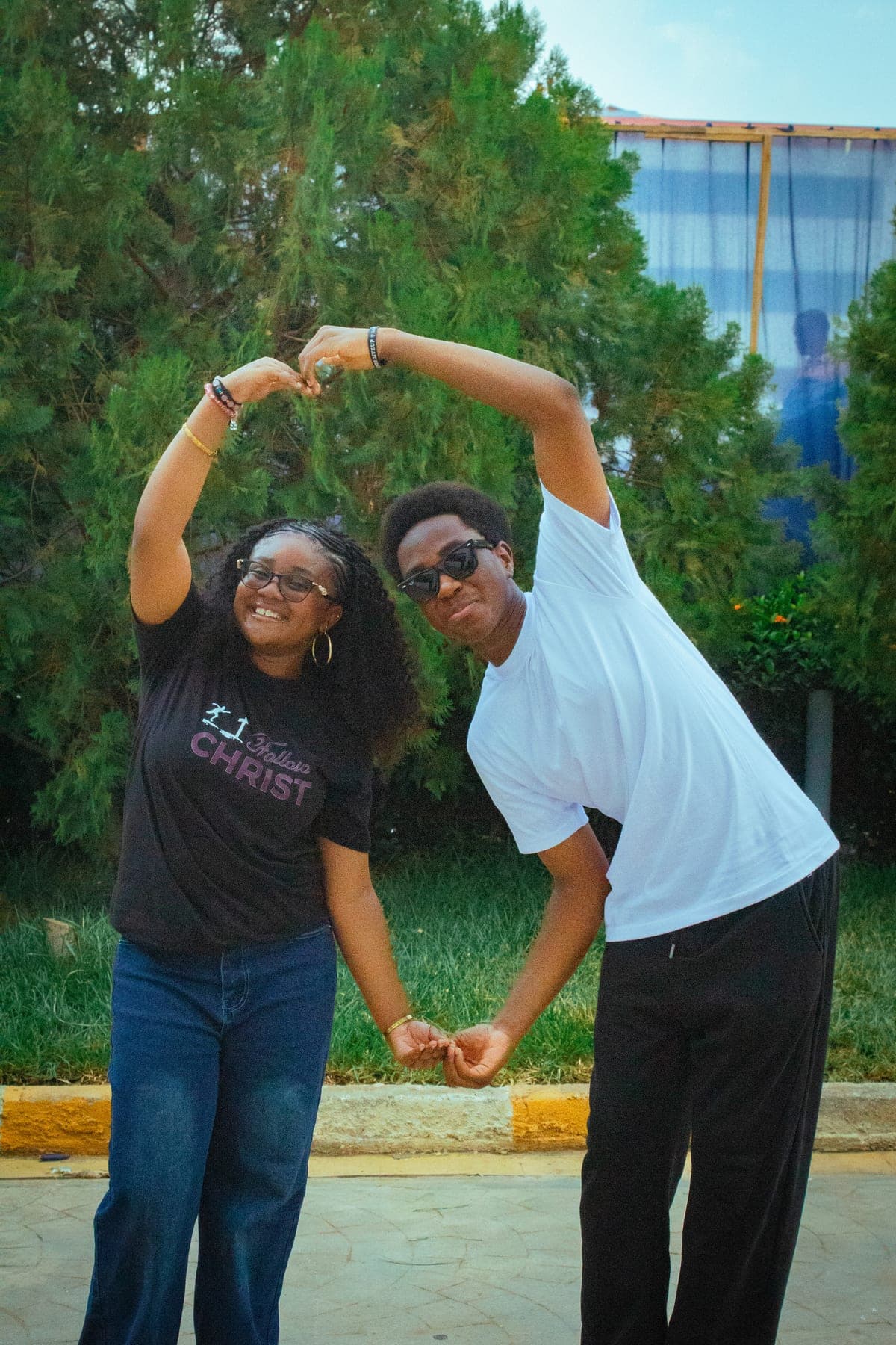Two students forming a heart shape with their arms, one wearing a Follow Christ t-shirt